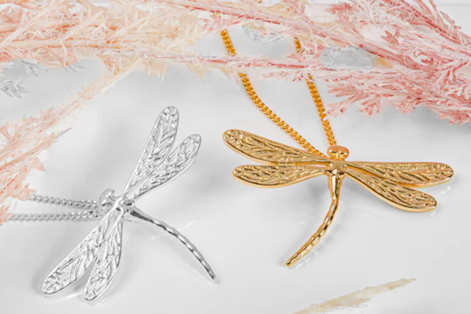 Gold and silver dragonfly-shaped pendants on a light background with pink decorative elements.